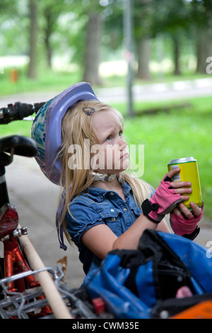 Infelice ragazza polacca i 4 anni di età con soda indossando rosa bicicletta senza dita guanti e casco. Paderewski Park Rzeczyca Polonia centrale Foto Stock