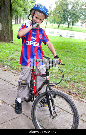 Ragazzo polacco di età di 8 in appoggio sulla sua bicicletta indossando il casco e guanti. Paderewski Park Rzeczyca Polonia centrale Foto Stock