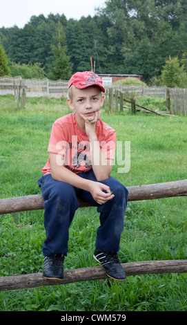 Ragazzo polacco età 10 dal villaggio seduto sul log recinzione che circonda un piccolo campo. Mala Wola Polonia centrale Foto Stock