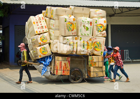 Chiudere orizzontale su di un carrello sovraccaricato con piena di scatole di cartone essendo spinto e tirato da donne lungo un tratto di strada in Cambogia. Foto Stock