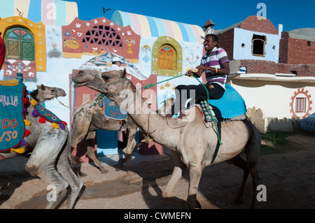 Gli abitanti di un villaggio nubiano cavalcare i cammelli di Gharb Soheil Nubian Village sulla sponda ovest del Nilo vicino a Aswan Egitto Foto Stock