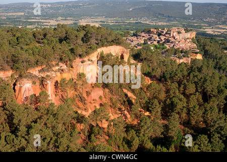 VISTA AEREA. Borgo medievale arroccato sulla cima di una scogliera di argilla ocra-rossa. Roussillon, Vaucluse, Provenza, Francia. Foto Stock