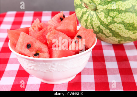 Pezzi di taglio fresco di anguria in una ciotola bianco su una tovaglia gingham. Foto Stock