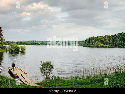 Il pescatore si siede su una tavola di legno posto barca sul lago in legno Foto Stock