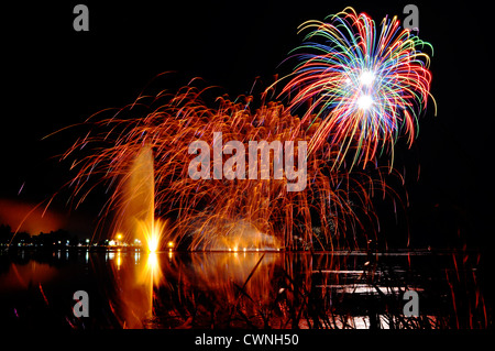 Impressionante, luminosi e colorati fuochi d'artificio su un lago con acqua di alleggerire la fontana grande festa dello sfondo. Foto Stock