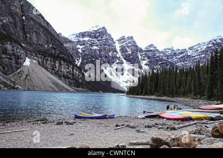 Un bel paesaggio dal Lago Moraine, Canada. Mostra il bordo del lago con le canoe in appoggio sulla riva, con montagne, foresta Foto Stock