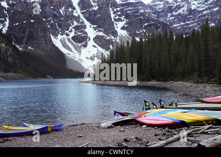Un bel paesaggio dal Lago Moraine, Canada. Mostra il bordo del lago con le canoe in appoggio sulla riva, con montagne, foresta Foto Stock