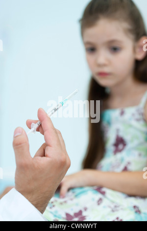 Medico la mano tenendo la siringa, ragazza seduta in background Foto Stock