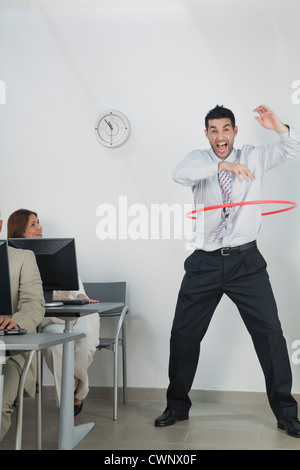 Giovane imprenditore giocando con hula hoop in office Foto Stock