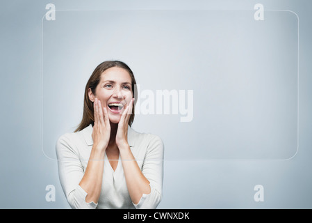 Donna che guarda la grande touch screen trasparente con espressioni di sorpresa sul viso Foto Stock