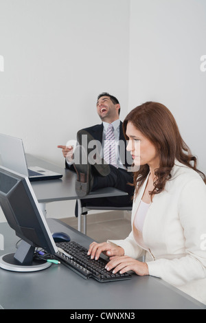 Imprenditrice lavorando in ufficio mentre collega ride in background Foto Stock