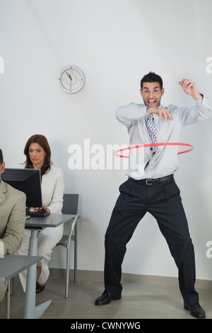 Giovane imprenditore giocando con hula hoop in ufficio mentre i colleghi il lavoro Foto Stock