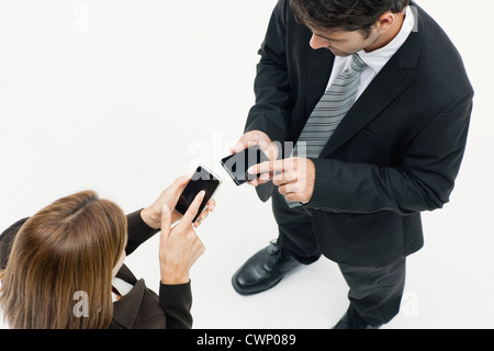 Imprenditrice e imprenditore in piedi faccia a faccia, entrambi gli smartphone utilizzando Foto Stock
