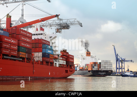 Porta occupata in scena a Rotterdam; navi portacontainer, rimorchiatore, eruttazione di fumo dalla nave di imbuto Foto Stock