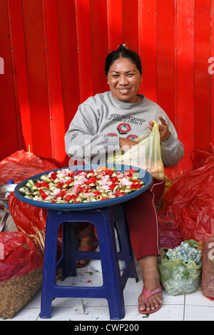 Un sorridente donna balinese facendo offerte che sono utilizzati come parte della religione indù. Mercati di Ubud, Bali, Indonesia Foto Stock