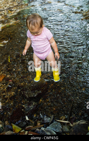 Baby girl indossare stivali di gomma, wading nel flusso Foto Stock