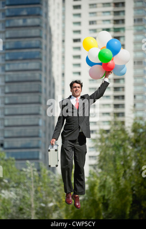 Imprenditore essendo portati via dal mucchio di palloncini Foto Stock