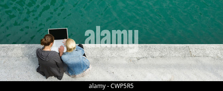 Giovani donne seduto accanto a canal, utilizzando il computer portatile insieme Foto Stock
