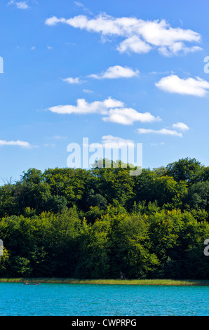 Bellissimo lungolago alberato con il motoscafo sotto nuvolosi cieli blu. Foto Stock