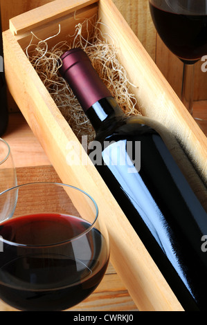 Un vino rosso bottiglia in una scatola di legno riempita di paglia su una sala di degustazione tavolo con due bicchieri di vino versato. Foto Stock