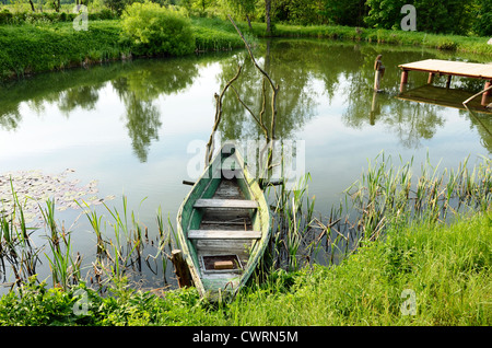 Vecchia barca di legno in piedi ormeggiato sulle rive dello stagno e ponte sotto l'acqua. Foto Stock