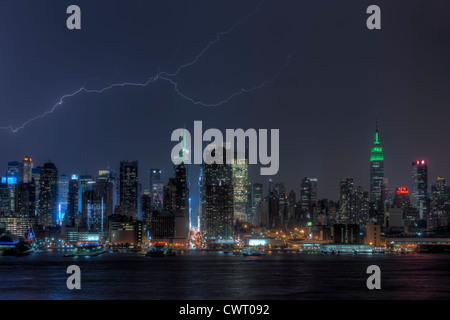 Una forcella di fulmine illumina il cielo di notte dietro il midtown skyline durante un temporale estivo in New York City. Foto Stock