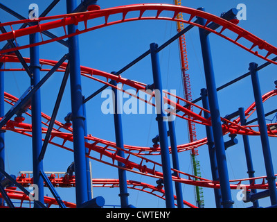 Chiudere fino in tracce di un twisty di blu e di rosso roller coaster contro un cielo blu. Foto Stock