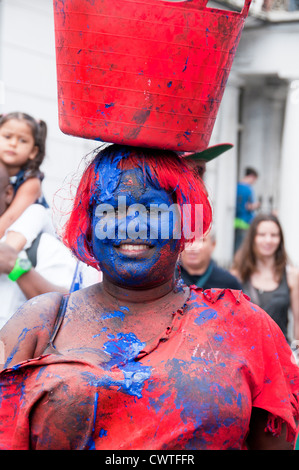 Ai partecipanti all Assemblea carnevale di Notting Hill 2012 rivestita con il rosso e il blu della vernice e portante una benna sulla sua testa Foto Stock