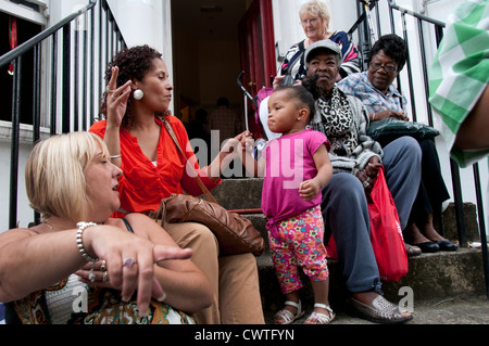 Famiglie seduti sui gradini di casa guardando la parata annuale al carnevale di Notting Hill 2012 Foto Stock