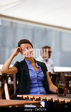 Piuttosto giovane donna seduta nel giardino di un ristorante Foto Stock
