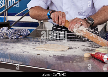 Un cuoco da co-operativa salviette per alimentare la pasta in eccesso dal suo perno di rotolamento durante la dimostrazione di come rendere le pizze fatte in casa. Foto Stock