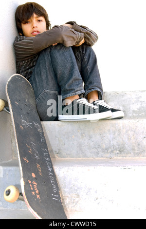 Ragazzo seduto su iniziative concrete con il suo skateboard oltre a lui Foto Stock