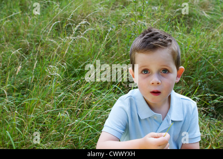 Little Boy in un campo di erba con un'espressione vuota Foto Stock