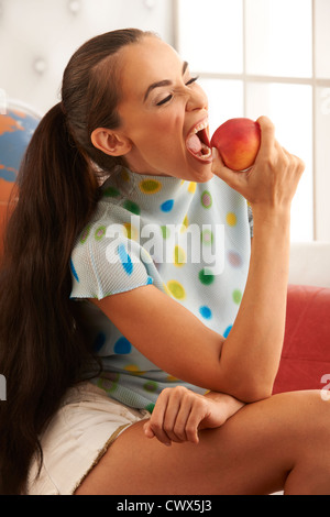 Bella bruna modello circa a mordere le pesche noci fresche per un snack sani in luminose e contemporanee home scena. Foto Stock