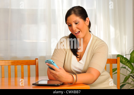 Attraente plus-dimensionato donna seduta nella luminosa sala azienda telefono cellulare. Foto Stock