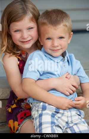 Carino giovane ragazza abbracciando il fratello minore sul patio passi a casa il giorno d'estate. Foto Stock