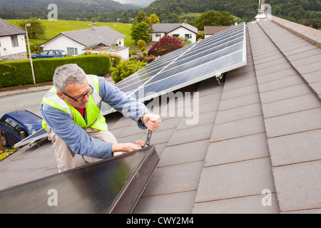 Un operaio montaggio solar pannelli termici per il riscaldamento di acqua e di un tetto di casa a Ambleside, Cumbria, Regno Unito, Foto Stock