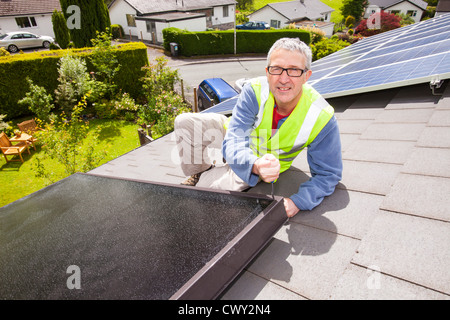 Un operaio montaggio solar pannelli termici per il riscaldamento di acqua e di un tetto di casa a Ambleside, Cumbria, Regno Unito, Foto Stock