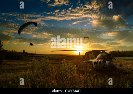 Elicottero schiantato nei campi e parapendio volare verso il tramonto. Foto Stock