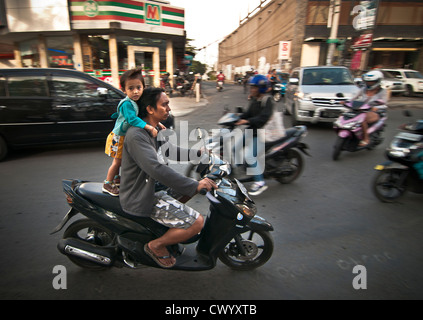 Bambino sulla schiena di un ciclomotore in Legian la strada principale di Legian, meridionale di Bali, Indonesia. Foto Stock