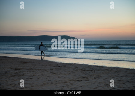 Surfista con la tavola da surf a Woolacombe Beach al tramonto Foto Stock