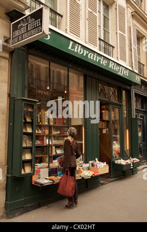 Una finestra-shopper sorge in punta di piedi per ottenere una vista migliore dei libri nella finestra della sponda sinistra del bookshop, Librairie Rieffel. Parigi, Francia. Foto Stock