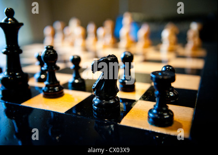 Legno intagliato pezzi di scacchi su una scacchiera in una luce calda. Foto Stock