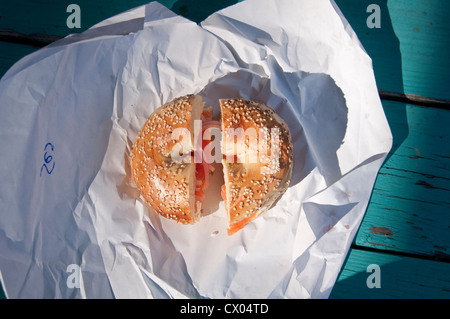 Un seme di sesamo bagel con lox (salmone affumicato), la crema di formaggio, cipolla e pomodoro, seduto su un involucro di carta, dalla struttura a molla bagel in Englewood, NJ. Foto Stock