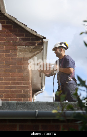 Workman perforazione di fori in una casa suburbana a parete in preparazione per la parete di cavità di isolamento Foto Stock