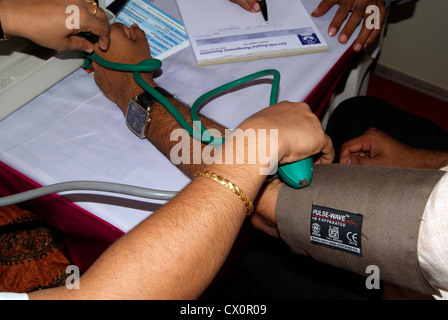 Medico controllando la pressione del sangue del paziente utilizzando il dispositivo di sfigmomanometro in ospedale in India Foto Stock