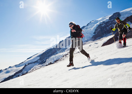 Un giovane uomo e donna correre e saltare giù il Muir campo di neve sul Monte Rainier, Washington, Stati Uniti d'America. Foto Stock