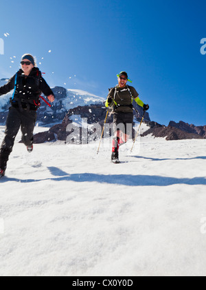 Un giovane uomo e donna in corsa verso il basso del Muir campo di neve sul Monte Rainier, Washington, Stati Uniti d'America. Foto Stock