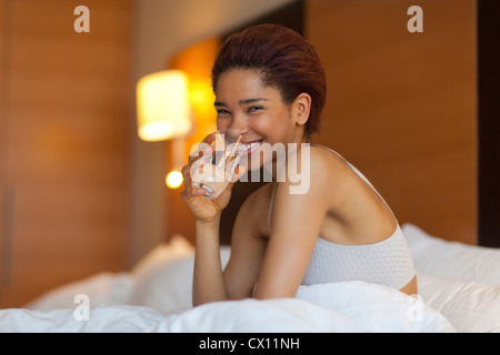 Giovane donna di bere un bicchiere di acqua nel letto Foto Stock