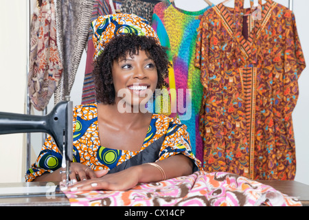 Bella americana africana sarto femmina che guarda lontano mentre la cucitura panno sulla macchina da cucire Foto Stock